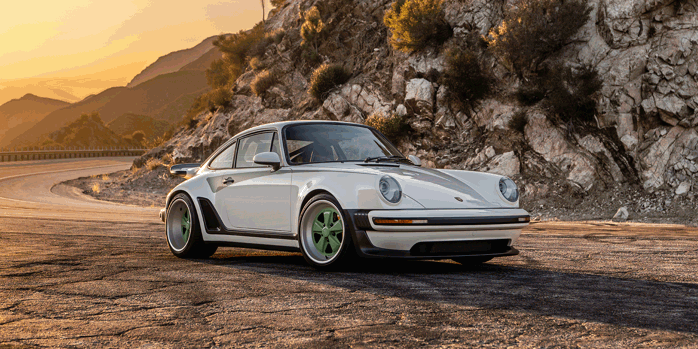 A white Porsche 911 with green wheel detail reimagined by Singer pictured on a mountain road at sunrise