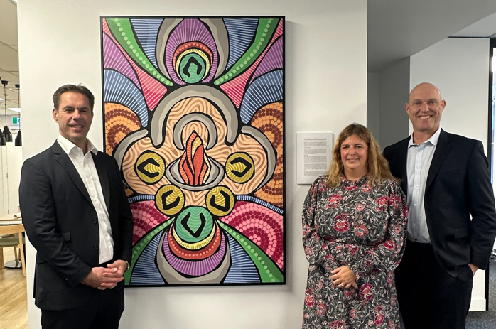 Graham Ritchie, Rachel White and Chris Hewitson standing in front of Ricardo's new reconciliation artwork by Arrernte artist Scott Rathman